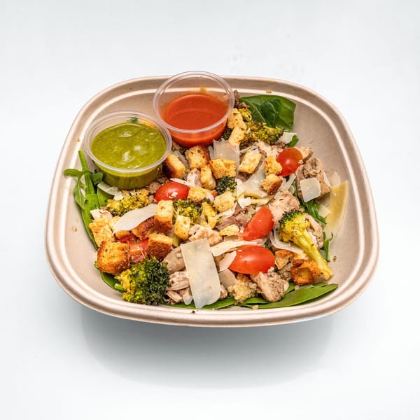 Chicken and broccoli salad with cherry tomatoes, croutons, and two dressing cups.