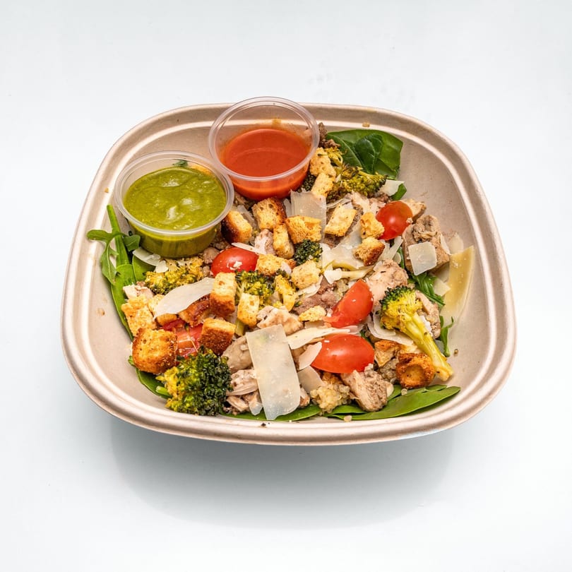 Chicken and broccoli salad with cherry tomatoes, croutons, and two dressing cups.