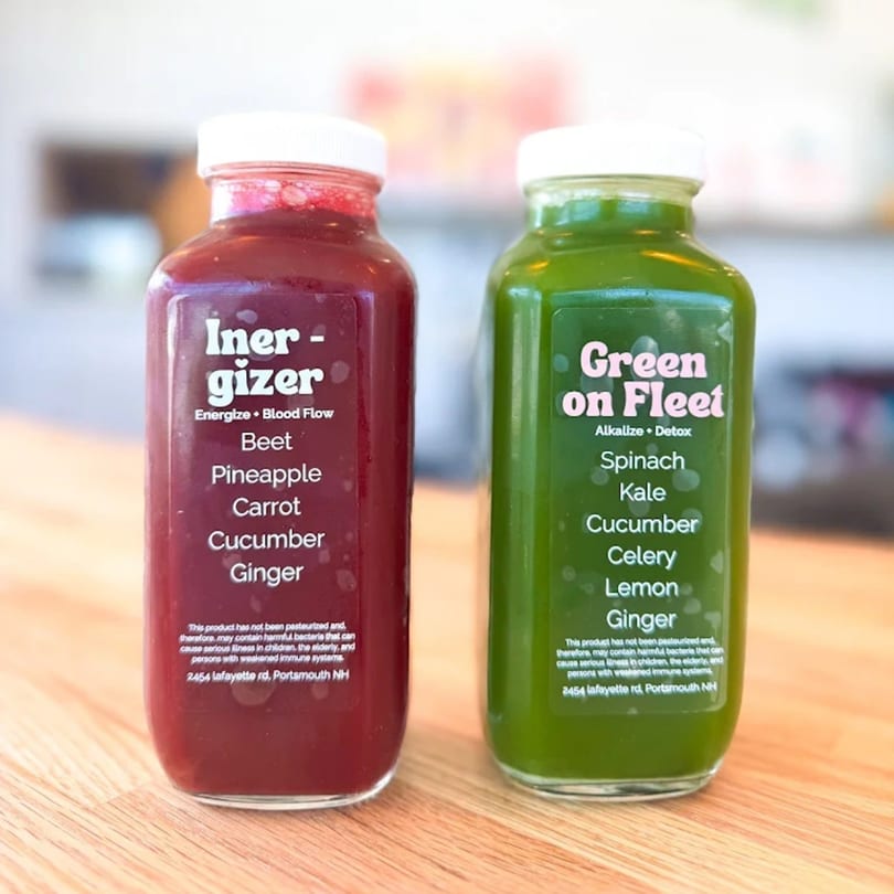 Two bottled juices, one red "Energizer" and one green "Green on Fleet", on a wooden surface.