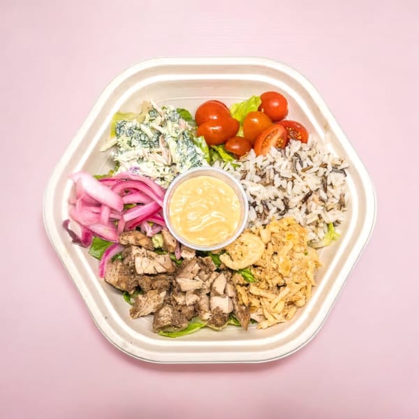 A hexagonal takeout container filled with chicken, rice, tomatoes, coleslaw, pickled onions, and sauce.