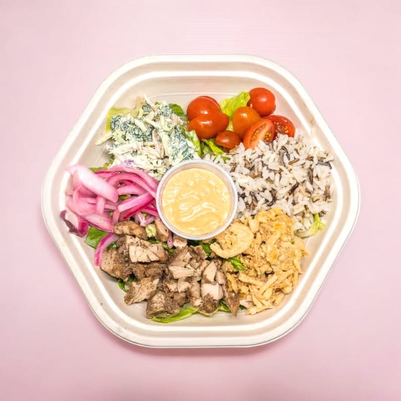 A hexagonal takeout container filled with chicken, rice, tomatoes, coleslaw, pickled onions, and sauce.