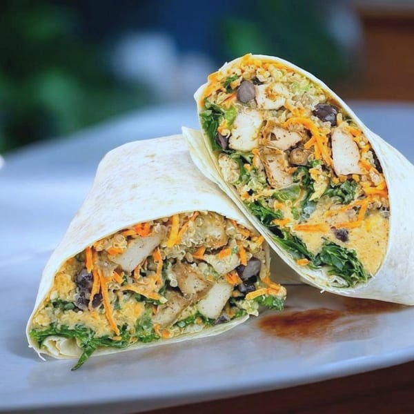Two halves of a chicken and vegetable wrap, filled with greens, carrots, and beans, on a white plate.