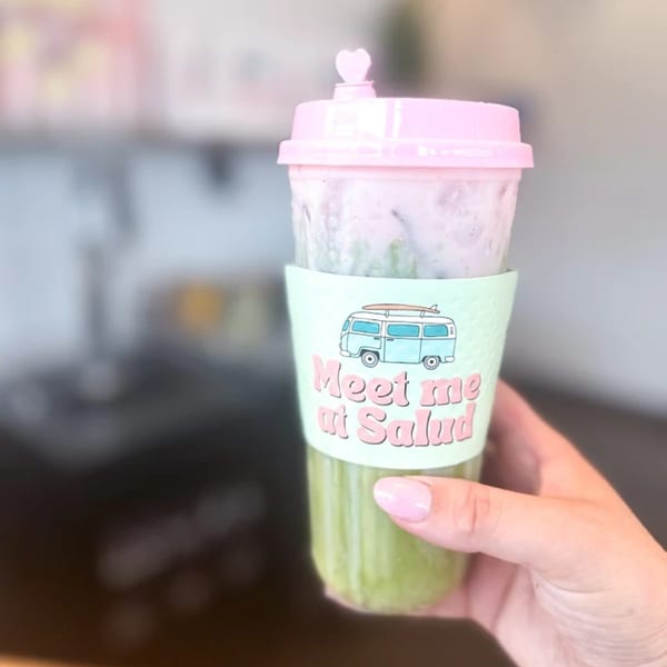 Hand holding a green drink with a pink lid and a "Meet me at Salud" sleeve.